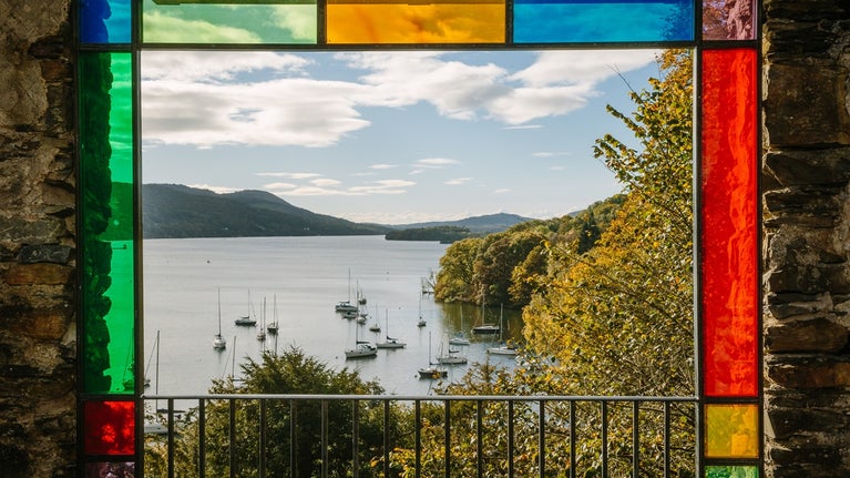 Claife viewing station's coloured glass panes in red, yellow , green and blue frame the view of Windermere and sailing boats